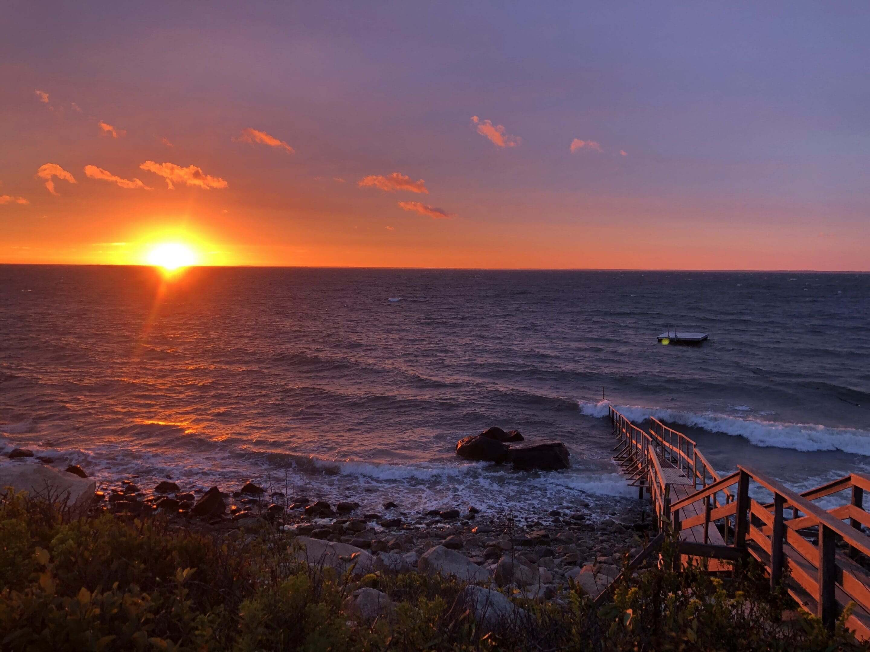 A sunset over the ocean with waves crashing on it.