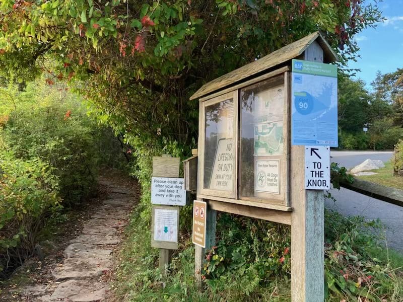 A trail sign and information board on the side of a path.
